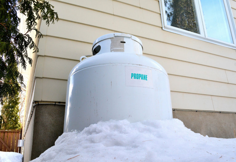 This shot shows a large propane fuel tank behind a residential building. The gas is used as fuel for home heating